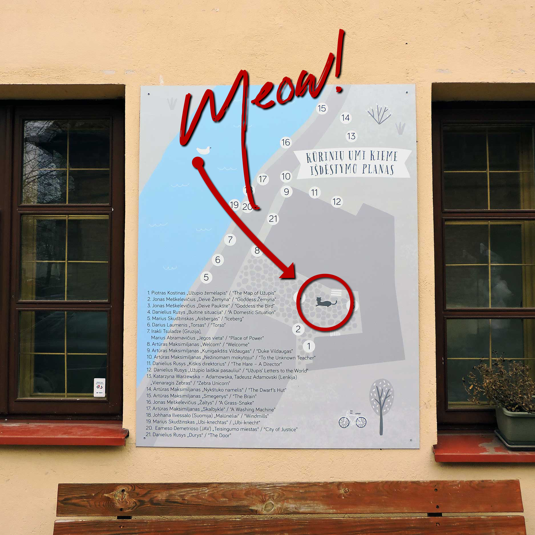 This image features a map labeled "Kลซriniลณ Umi Kieme Iลกdฤstymo Planas" (Layout Plan of Works in the Yard) mounted on a wall beside a window. A red arrow with the handwritten word "Meow!" points to a cat icon on the map, humorously marking its location. The list below identifies numbered points on the map, adding a playful and creative element to the scene.