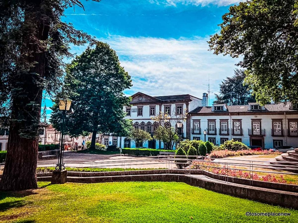 This image depicts a serene park setting, framed by lush greenery and historic buildings in the background. The scene captures a beautifully manicured garden with vibrant flower beds and neatly trimmed grass, set against a backdrop of charming, classic architecture. The bright blue sky and dappled sunlight create a peaceful atmosphere, making it ideal for highlighting quiet, picturesque spots perfect for leisurely strolls or slow exploration in a European town. This setting would work wonderfully in content focusing on peaceful urban parks, off-the-beaten-path destinations, or the charm of European small towns. Let me know if you’d like to explore more ways to use this image!